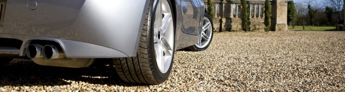 Silver sports car parked on a gravel driveway beside a stone balustrade in an English country garden.